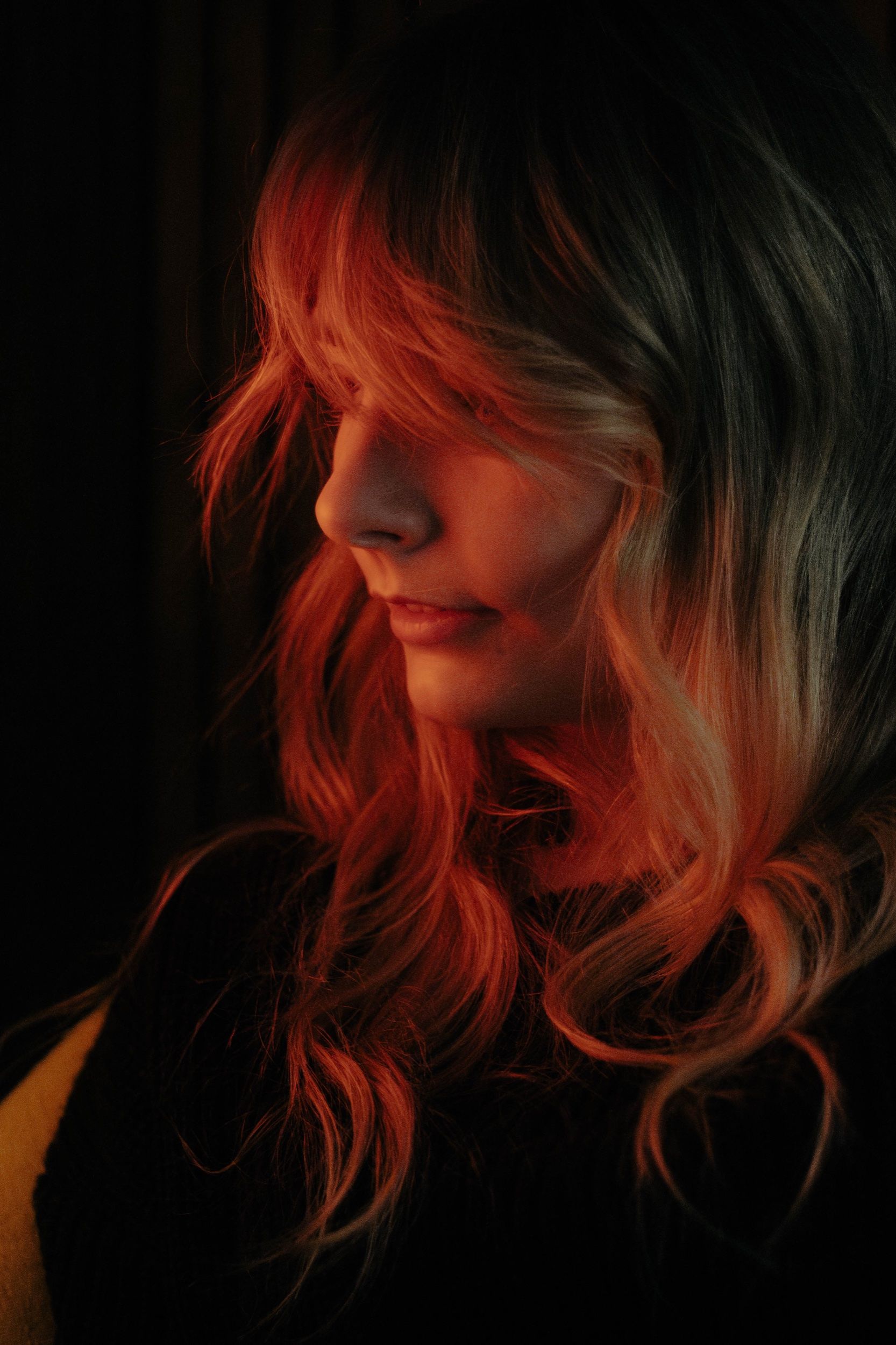 Nikola in profile, hair lit by warm red light against a dark background